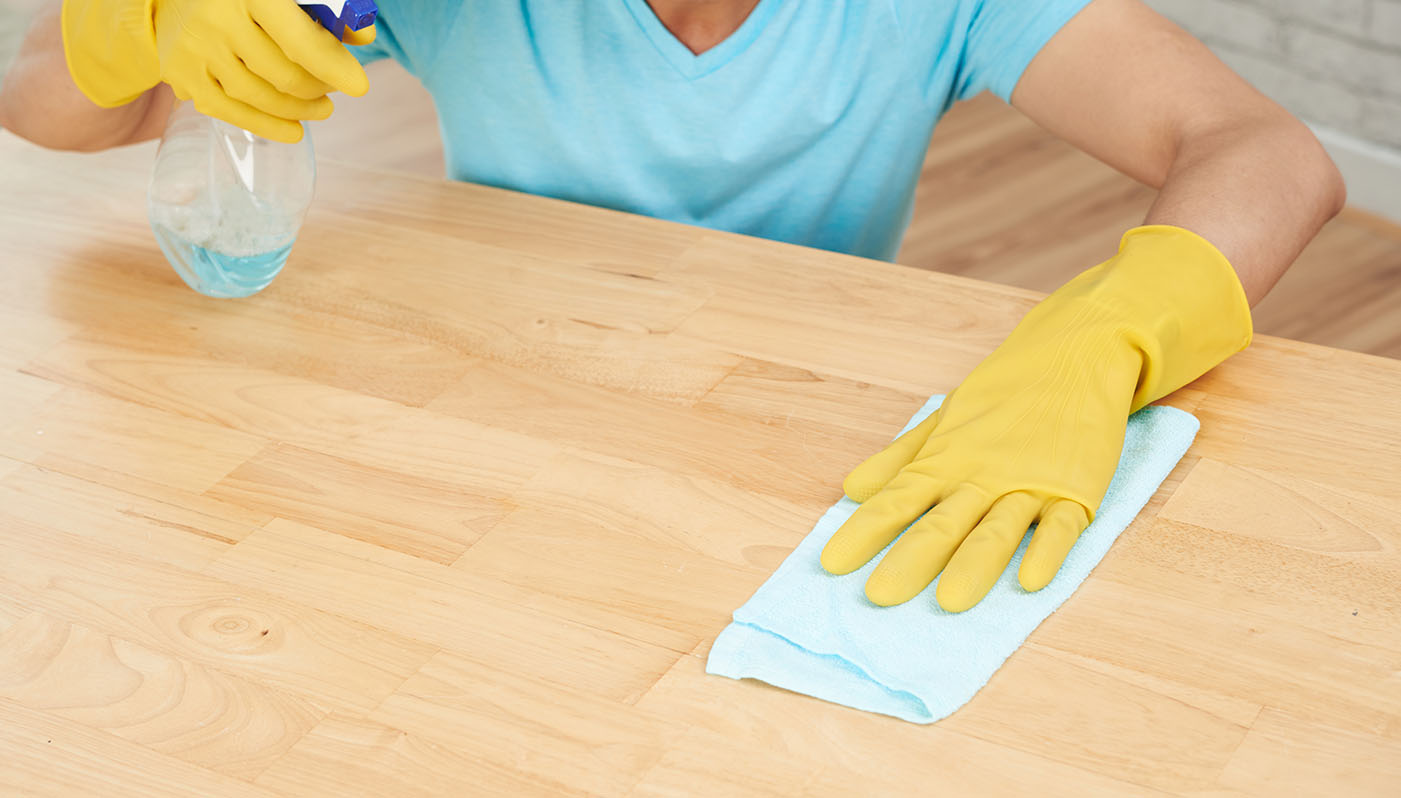 woman is using a spray bottle and a microfiber cloth to clean a table