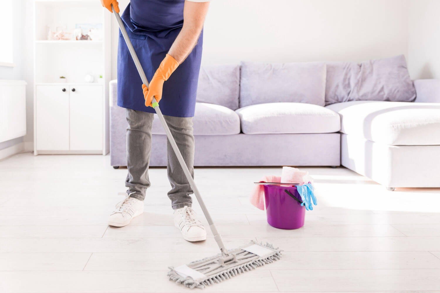 professional cleaner is mopping the floor with a basket full of cleaning tools